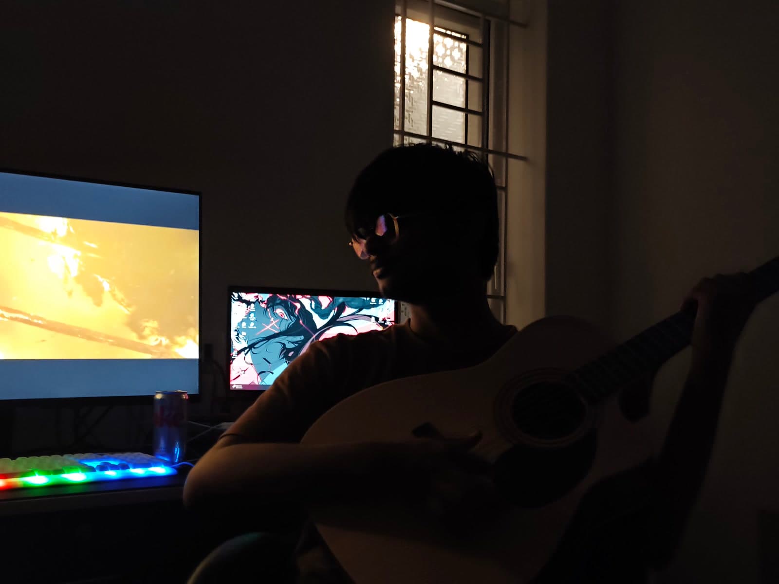 Sri playing guitar at a desk, monitors glowing behind